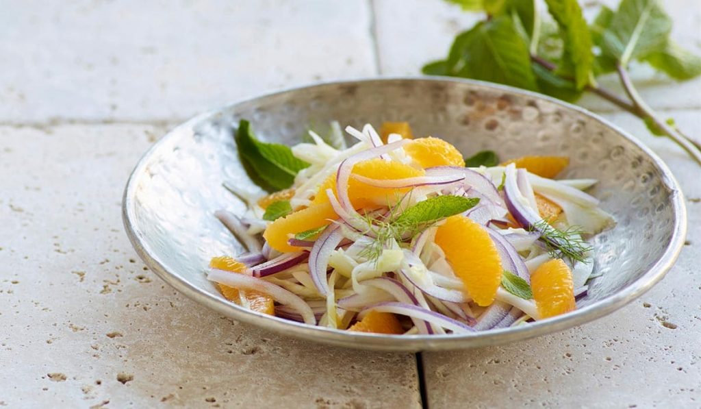 Bol de ensalada vegana en mesa con naranja y berros rica en hierro